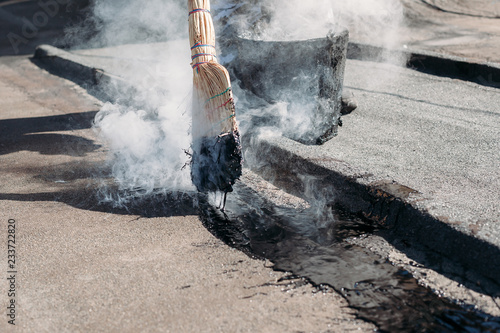 Worker repairs the roof with molten tar from a bucket with a broom.