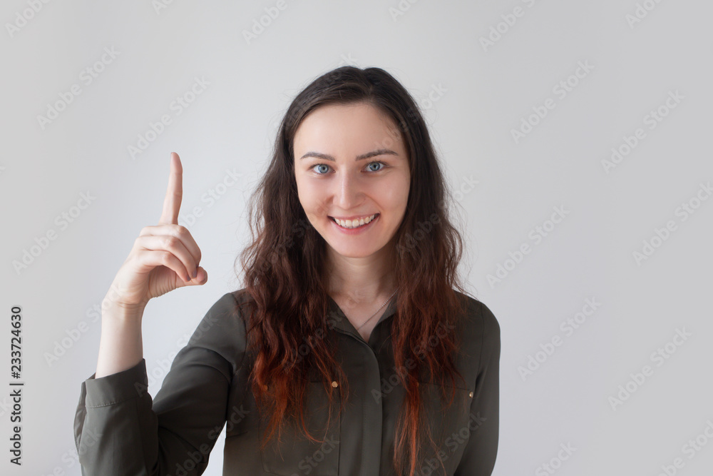 Happy pretty Caucasian girl raising one finger and smiling. Young specialist having brilliant thoughts. Creative teacher concept Happy pretty Caucasian girl raising one finger and smiling. Young specialist having brilliant thoughts. Creative teacher concept