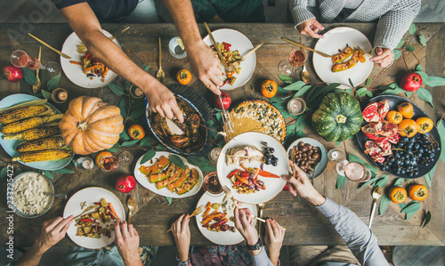 Traditional Thanksgiving or Friendsgiving holiday celebration party. Flat-lay of friends feasting at Thanksgiving Day table with turkey, pumpkin pie, roasted seasonal vegetables and fruit, top view