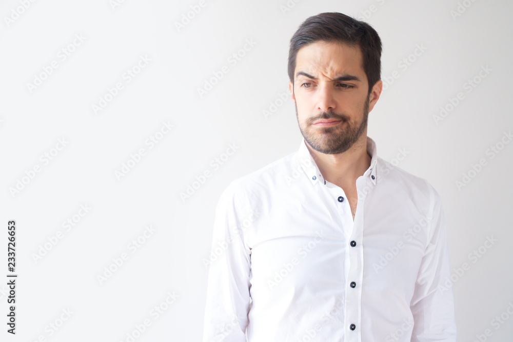 Skeptic young Caucasian businessman frowning and looking aside. Portrait of attractive man in white shirt deeply thinking. New project concept Skeptic young Caucasian businessman frowning and looking aside. Portrait of attractive man in white shirt deeply thinking. New project concept