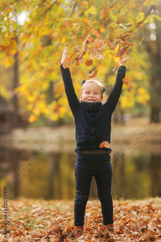 Beautiful young girl sist in leaves and throws them up. Colorful background. Happy little girl smile and have fun