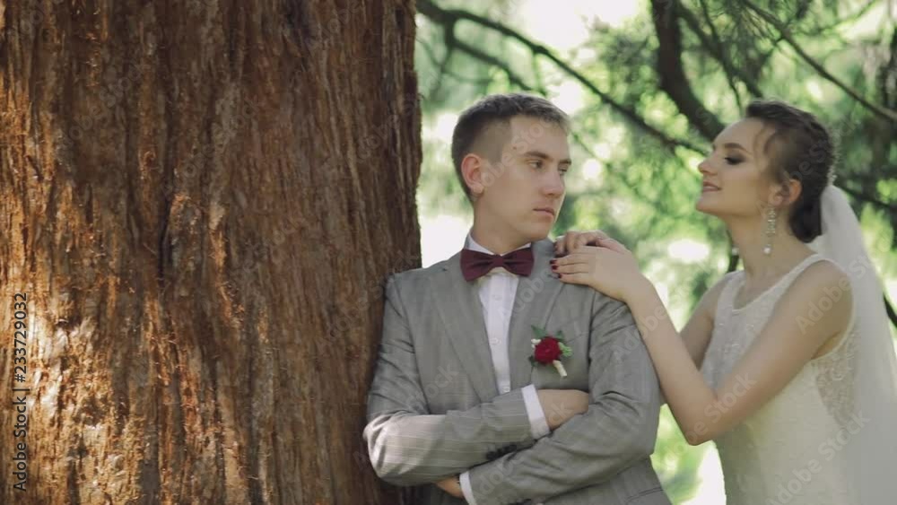 Young and beautiful wedding couple together in the park near big tree. Lovely groom and bride. Wedding day. Slow motion Young and beautiful wedding couple together in the park near big tree. Lovely groom and bride. Wedding day. Slow motion