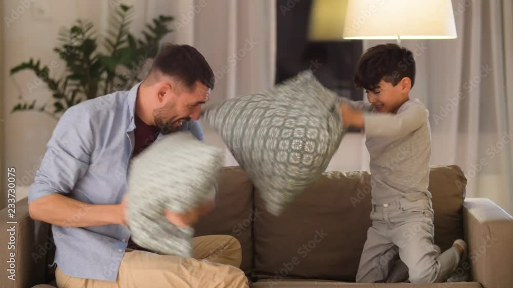 family, childhood and fatherhood concept - happy father and little son fighting by pillows having fun on sofa at home family, childhood and fatherhood concept - happy father and little son fighting by pillows having fun on sofa at home