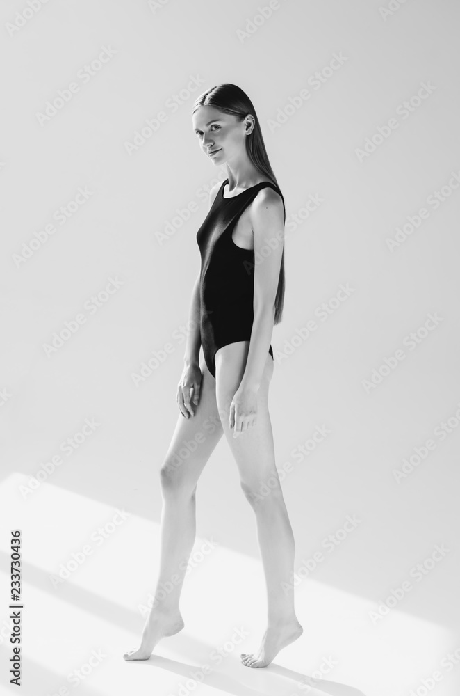 Naklejka premium Black and white shot of Fashionable young woman posing in black bodysuit, on grey