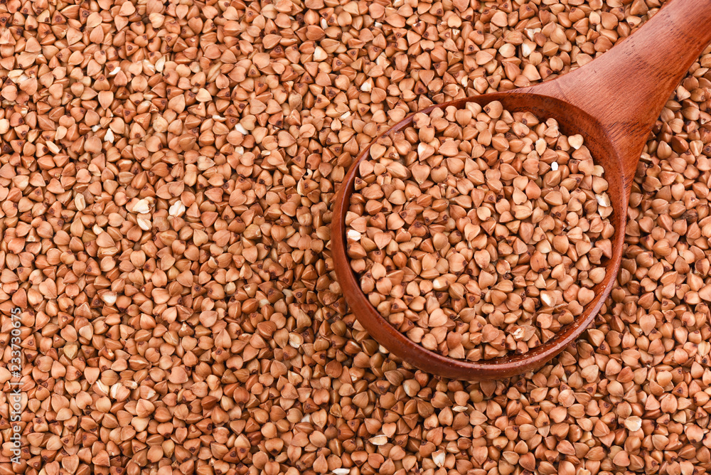 Obraz premium A wooden spoon full of buckwheat among the buckwheat. Top view