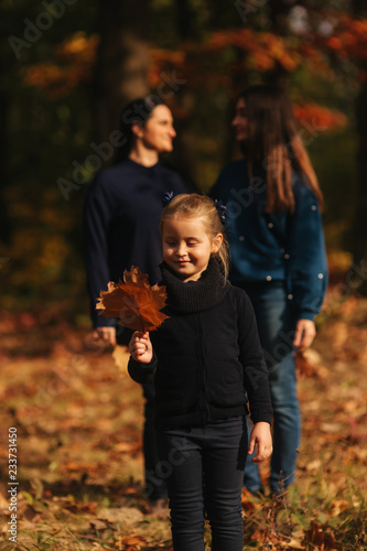 Little girl collect leaves in the forest. Background of mom dad and sister. Young family in autumn park