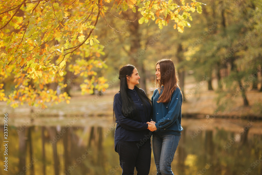 Mother with ldedt daughter stand in front of lake in the park. Yellow tree in autumn time Mother with ldedt daughter stand in front of lake in the park. Yellow tree in autumn time