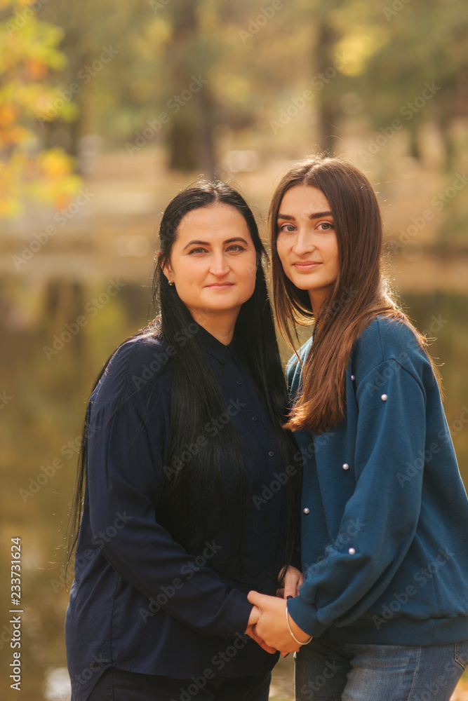Fototapeta premium Mother with ldedt daughter stand in front of lake in the park. Yellow tree in autumn time