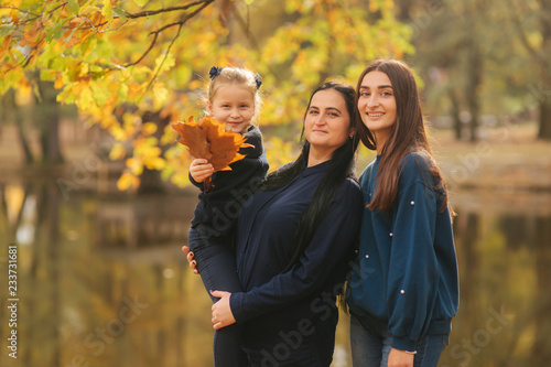 Mom and two daughter have fun in ther park. Youngest daughter collect leaves and smile. Happy family walking in the forest