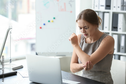 Photography Young woman suffering from pain in elbow at workplace