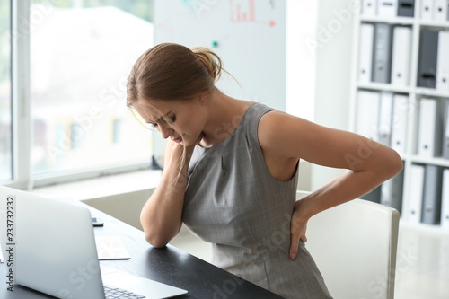 Young woman suffering from back pain in office