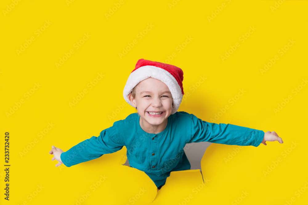 Happy child in Santa red hat is breaking through color paper wall. Happy child in Santa red hat is breaking through color paper wall.