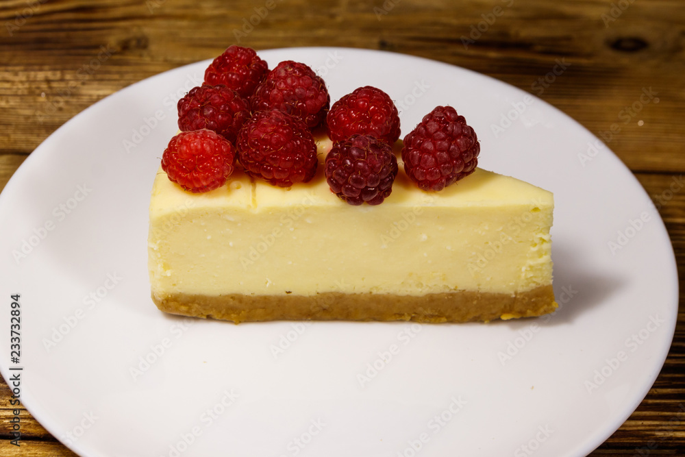 Piece of tasty New York cheesecake with raspberries in a white plate on wooden table Piece of tasty New York cheesecake with raspberries in a white plate on wooden table