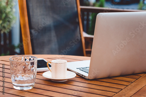Laptop, a glass of coffee and a glass of water on a wooden table on a terrace, a place for business work outside and productivity 