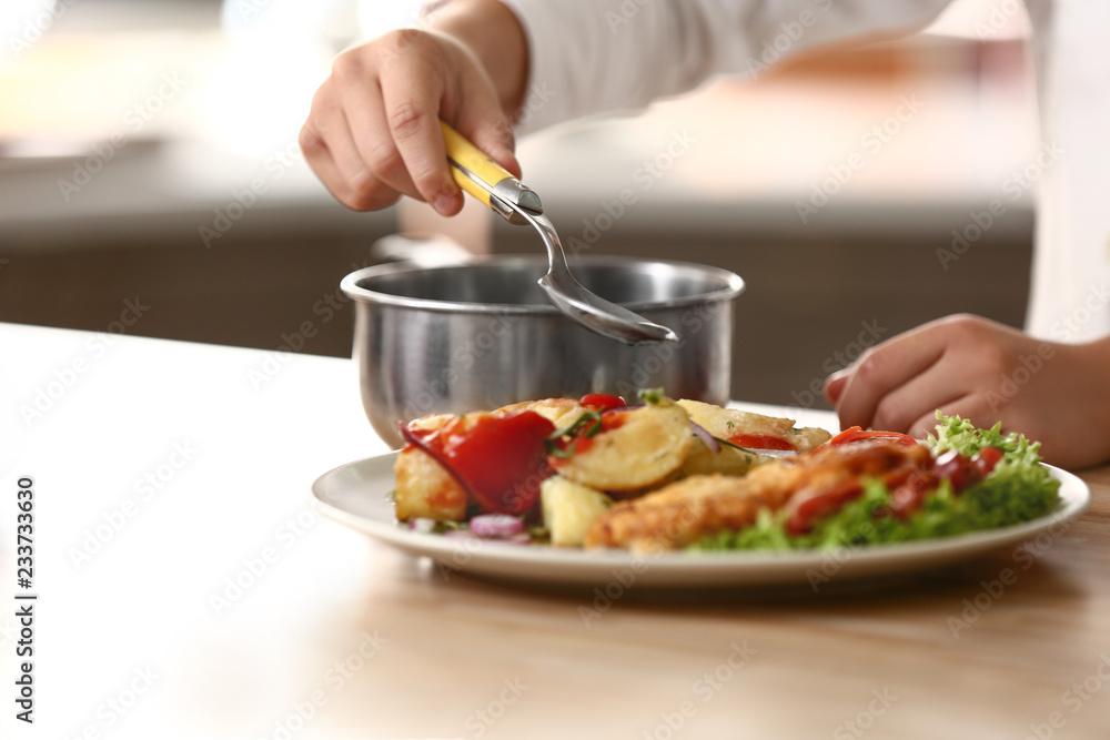 Cute little chef dressing tasty dish in kitchen, closeup Cute little chef dressing tasty dish in kitchen, closeup
