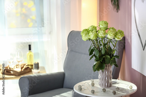 Vase with beautiful green roses on white table in room