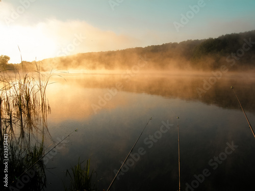 Beautiful red sunrise over the lake with fog and fishing rods