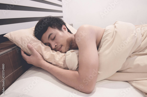 Young Asian man smiling and hugging the blanket while sleeping in his bed at home.