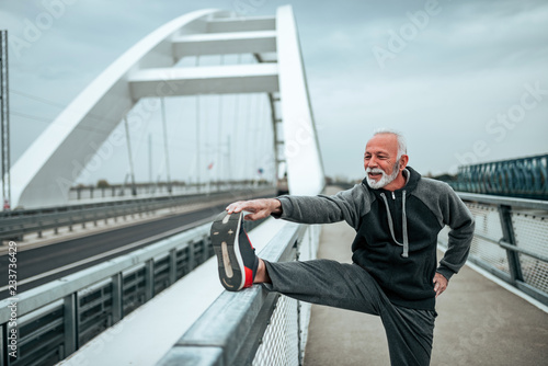 Senior sportsman stretching outdoors, on the city bridge.