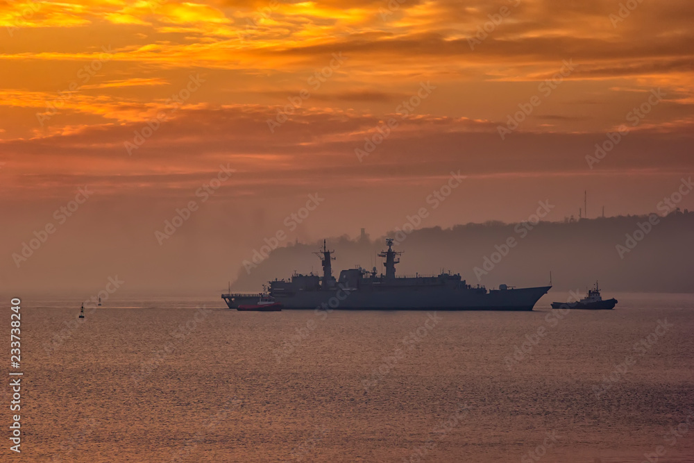 Military Battleship using tugs go to the port at the sunrise time