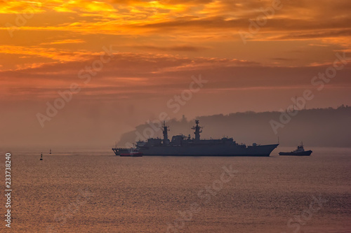 Photography Military Battleship using tugs go to the port at the sunrise time