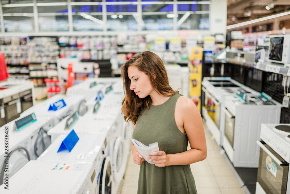 Woman buys washing machine in a store, holding manual.
