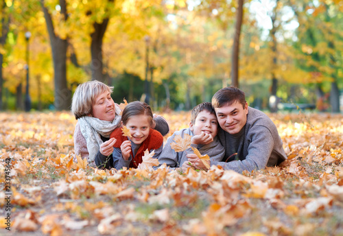 Happy family lies in autumn city park on fallen leaves. Children and parents posing, smiling, playing and having fun. Bright yellow trees. © soleg