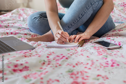 Woman sitting on bed at home working, partial view