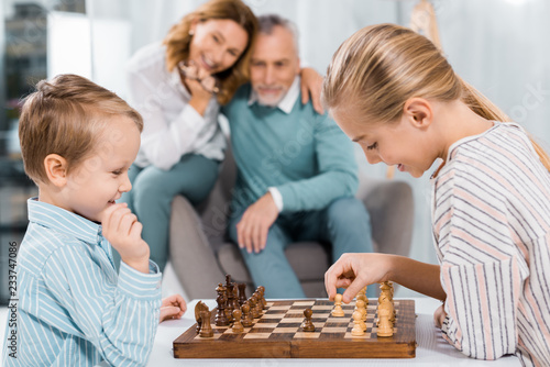 side view of happy kids playing chess while their grandparents sitting near at home