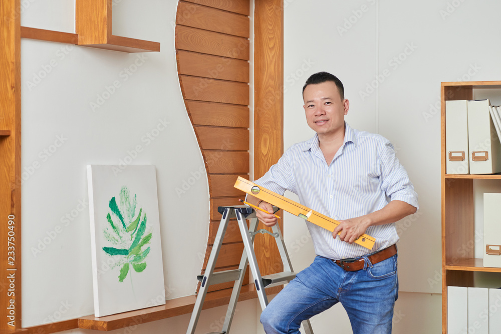 Portrait of confident man standing with level and decorating the wall with picture