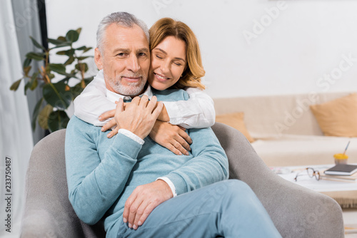 attractive woman with closed eyes embracing middle aged husband at home