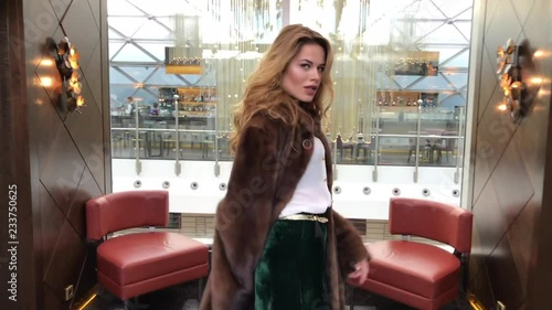 Young slim blonde woman in mink coat posing in the lobby of an expensive hotel