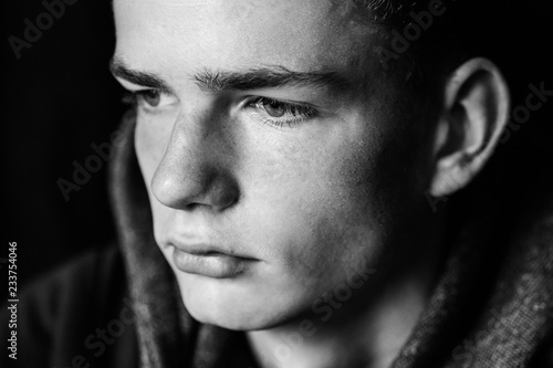 portrait of a serious teenage boy on a dark background, teenage problem concept, black and white photo
