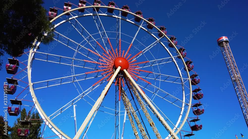 Giant ferris wheel spinning in time lapse in spinning ride roller coaster attraction amusement park on clear blue sky Giant ferris wheel spinning in time lapse in spinning ride roller coaster attraction amusement park on clear blue sky