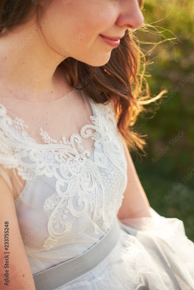Smiling bride holding edge of dress, sunny day, close-up Smiling bride holding edge of dress, sunny day, close-up