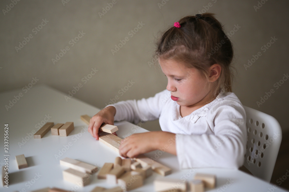 Sad child girl builds of wooden constructor Sad child girl builds of wooden constructor
