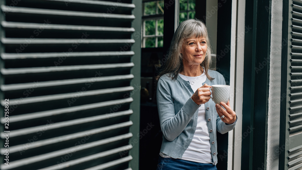 Fototapeta premium Senior woman standing at the door holding a coffee cup