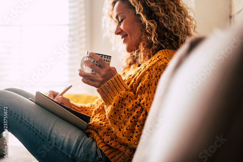 Happy cute lady at home write notes on a diary while drink a cup of tea and rest and relax taking a break. autumn colors and people enjoying home lifestyle writing messages or lists.  photo