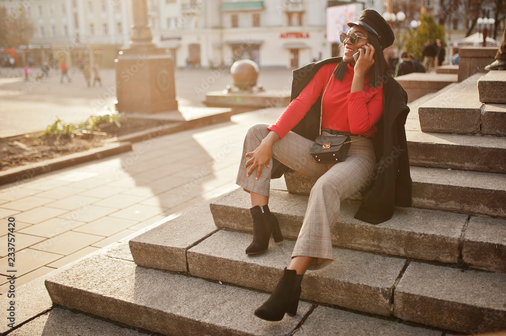 African american fashion girl in coat and newsboy cap, sunglasses posed at street. African american fashion girl in coat and newsboy cap, sunglasses posed at street.