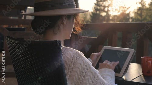 Woman traveler sits at the terrace with a tablet against beautiful mountain scenery during journey. Concept of freelance or remote business, blogger, writer.