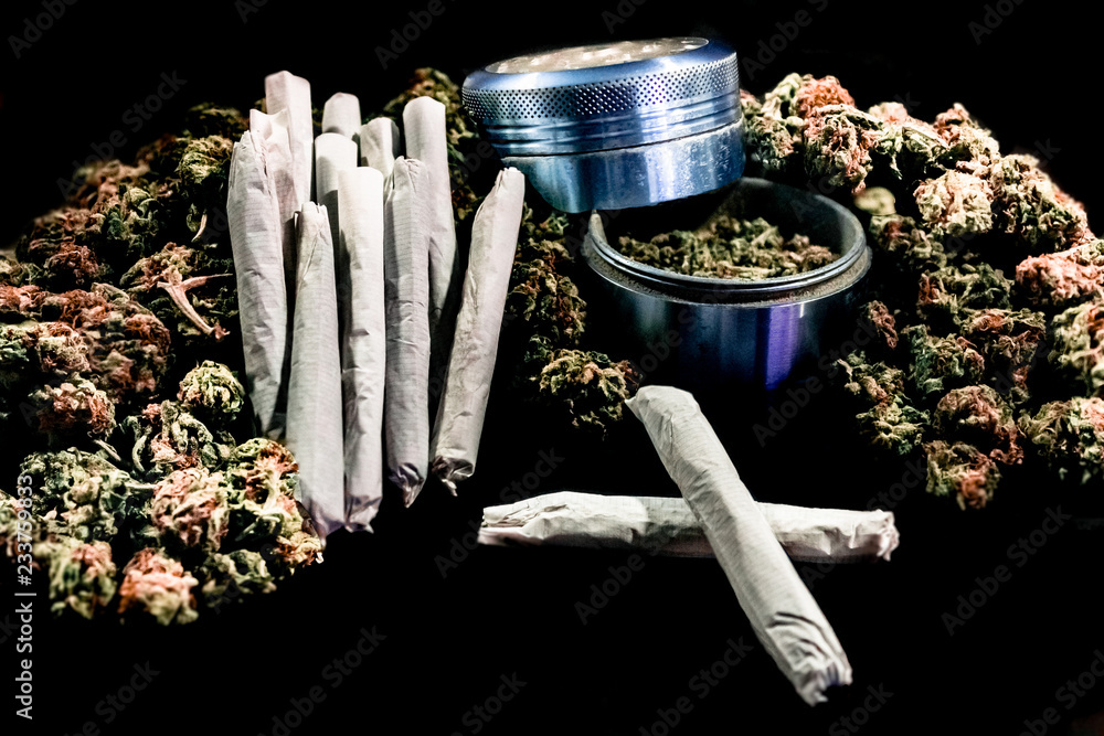 Marijuana joints stacked on a pile of bud with a cobalt coloured bud grinder.