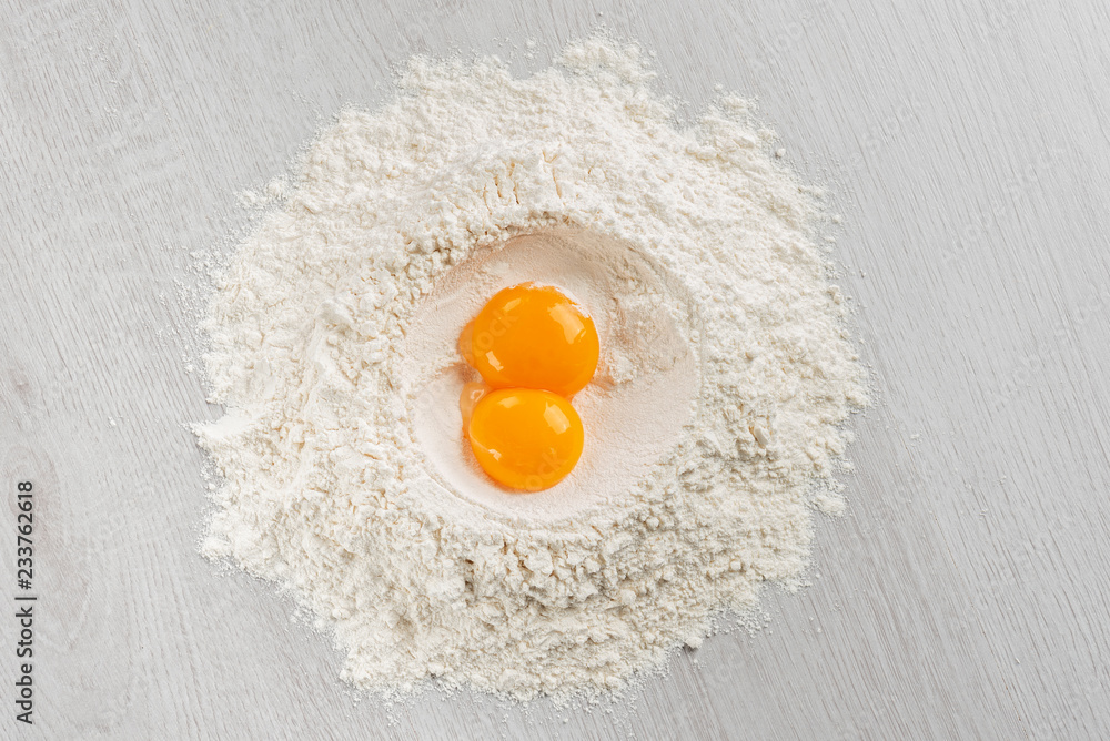 pile of flour with egg yolks for dough on table, top view. pile of flour with egg yolks for dough on table, top view.