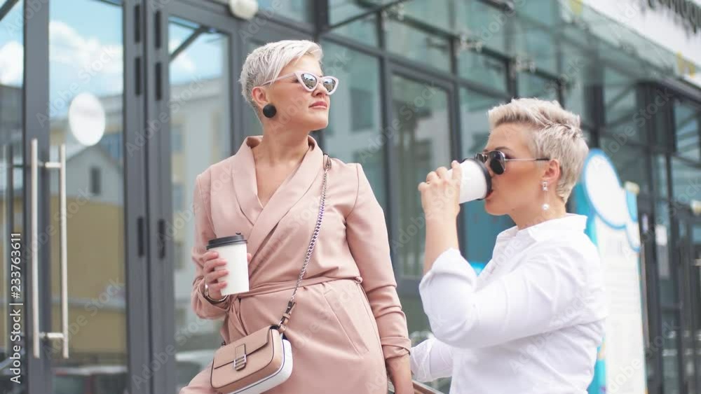 Happy businesswomen with coffee cup conversing outside office building Happy businesswomen with coffee cup conversing outside office building