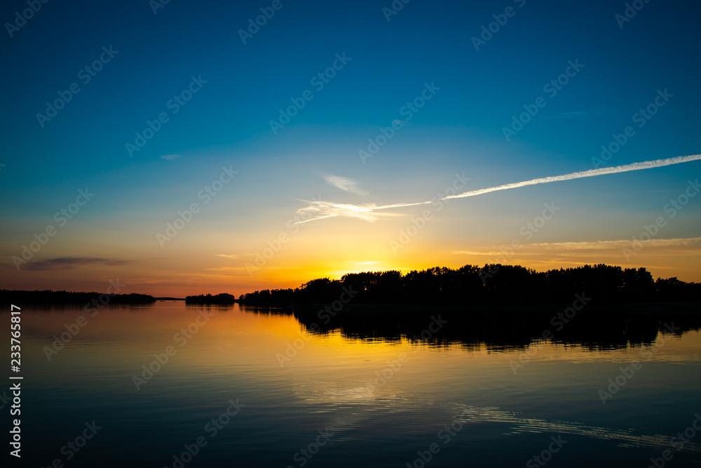 A beautiful and calming sunset accented by a long narrow cloud, a few days after midsummer, reflected on the water of a cove on the Island of Nicklösa in the Åland Islands, Finland.