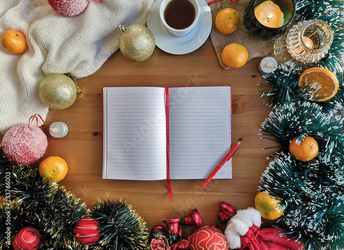 An open empty notebook on the wooden background with christmas and new year decoration, candles, oranges, christmas balls and cup of coffee