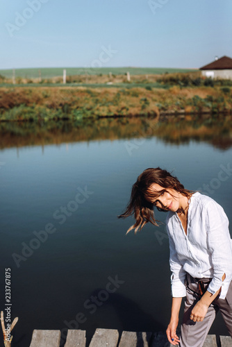 Portrait of beautiful woman near a wooden bridge by the lake at sunny day. Atmospheric portrait of a lonely girl walking