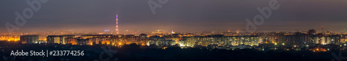 Wide panorama, aerial night view of modern tourist Ivano-Frankivsk city, Ukraine. Scene of bright lights of tall buildings, high television tower and green suburbs on Carpathian mountains background.