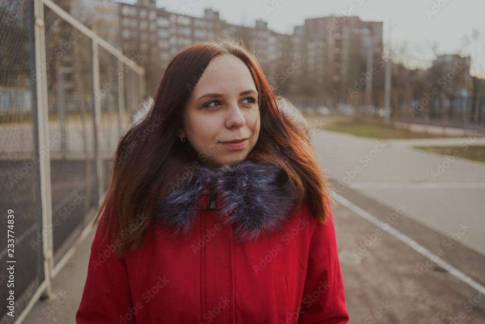Happy beautiful young girl in a red jacket posing outside on a cloudy day. emotional portrait of a student. street style