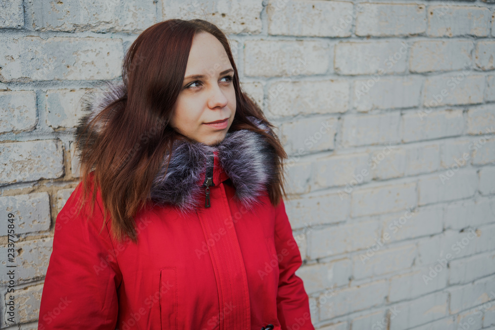 Happy beautiful young girl in a red jacket posing outside on a cloudy day. emotional portrait of a student. street style