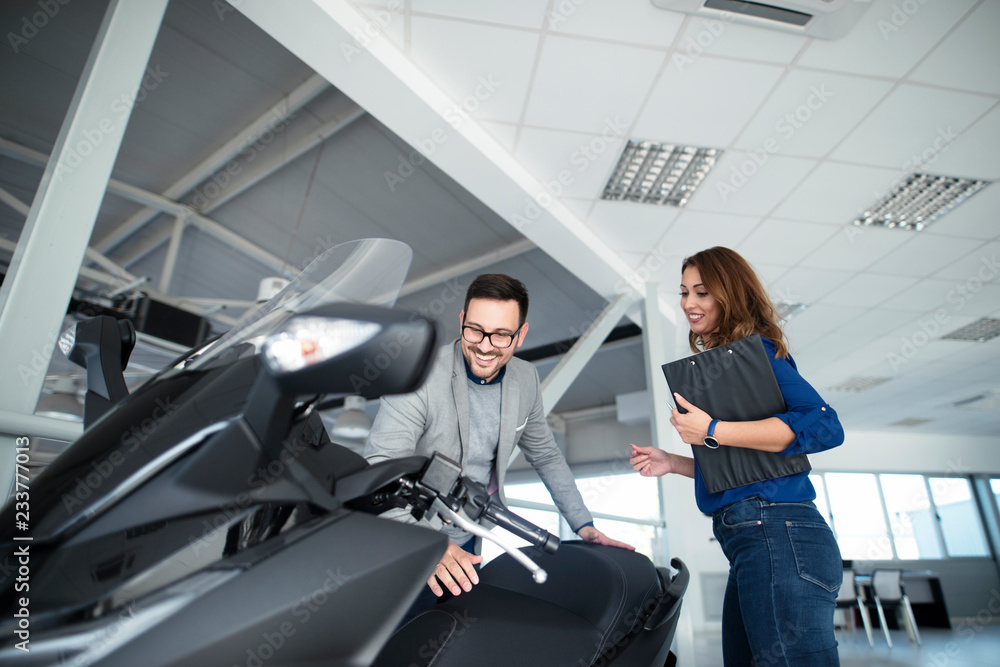 Fototapeta premium Mężczyzna kupuje nowy motocykl w salonie dealerskim pojazdu z pomocą atrakcyjnej sprzedawczyni.
